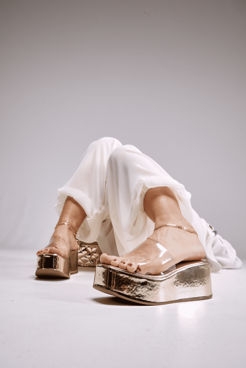 tamanco-flatform-feminino-tira-vinil-dourado-adele Adele - Tamanco Flatform Feminina Tira Vinil Dourado nos pés da modelo sentada no chão, pernas esticadas