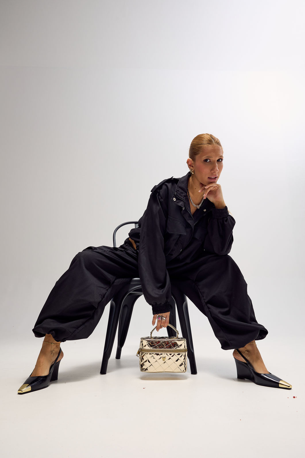Slingback Naomi Preto com Look Modelo usando slingback feminino Naomi preto com salto anabela e bico metálico dourado, combinado com look preto e bolsa metalizada dourada.