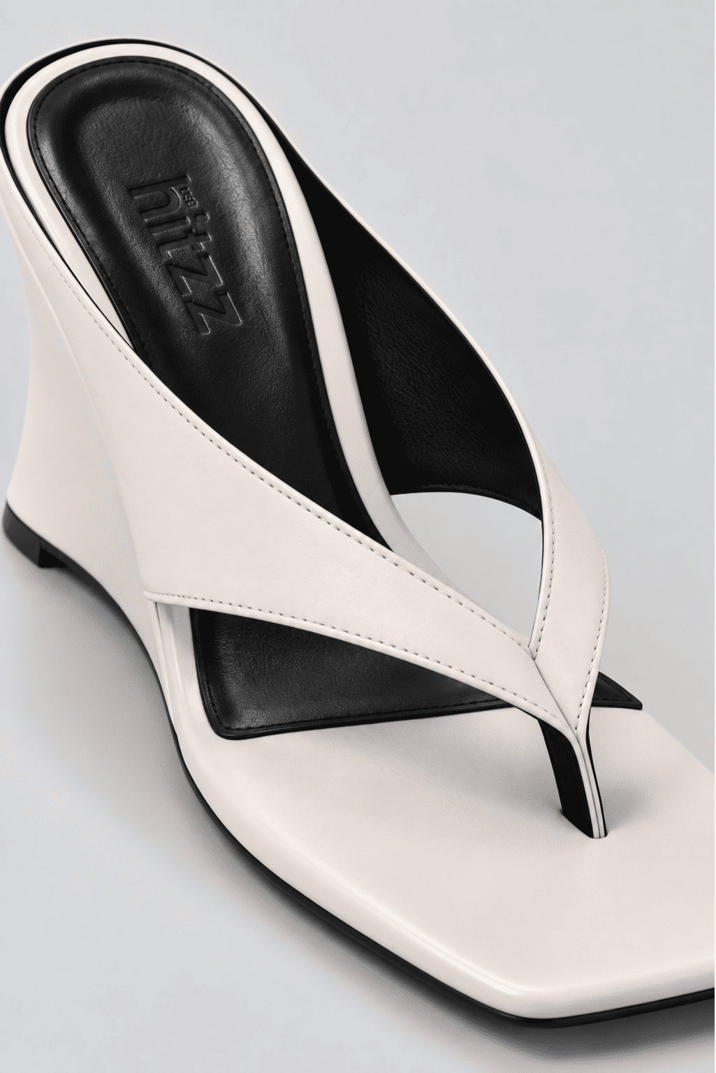 tamanco-feminino-dedo-salto-anabela-off-white-misaki Close do tamanco dedo off white, destacando a tira flip flop e a palmilha preta com a marca hitzz gravada.