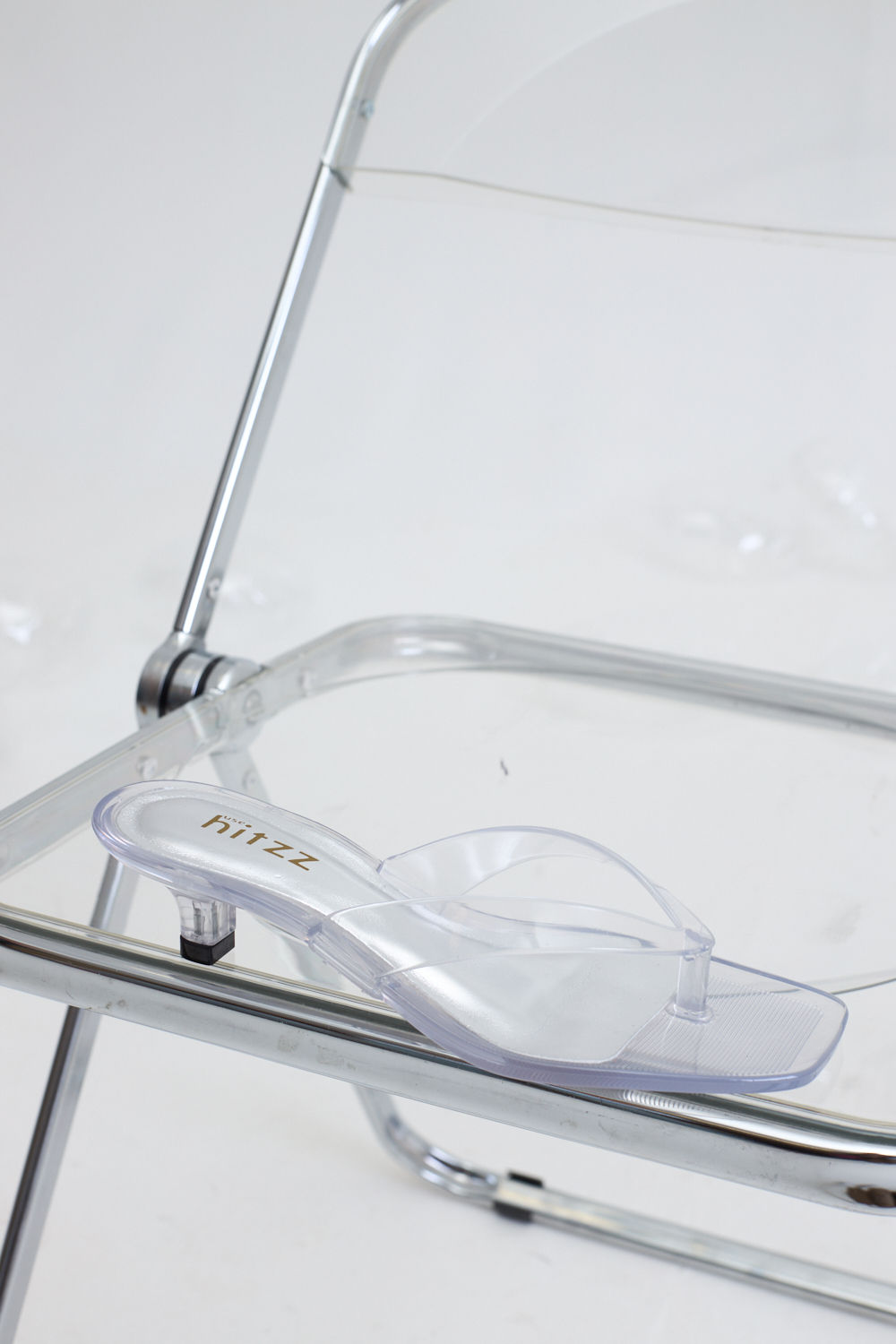 gummy-tamanco-feminino-transparente-salto-baixo Tamanco Feminino Flip Flop Gummy transparente em PVC sobre cadeira metálica, vista superior destacando as tiras e o bico quadrado