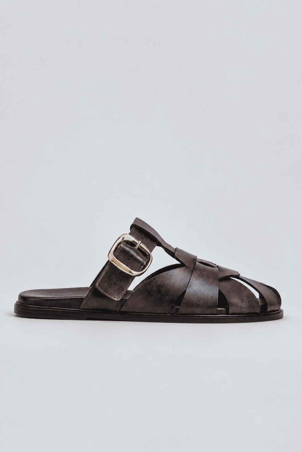 clog-feminino-fivela-marrom-aura Clog feminino marrom com tiras entrelaçadas e fivela dourada, sola preta rasteira, vista lateral, isolado em fundo cinza claro.