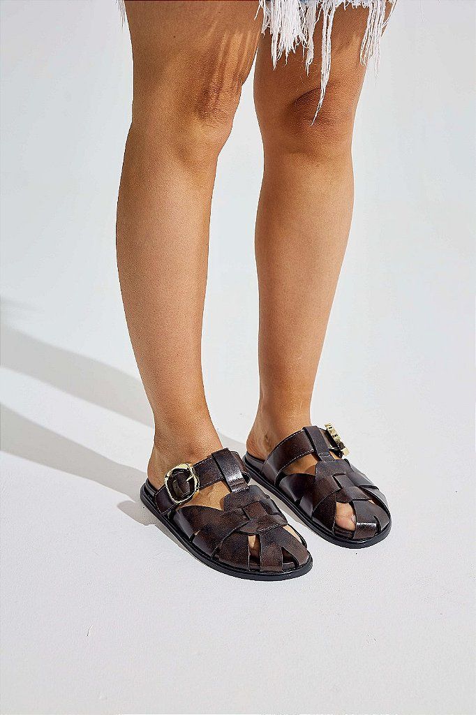 clog-feminino-fivela-marrom-aura Pernas femininas usando o clog marrom com fivela dourada, vista de frente, fundo claro em estúdio.