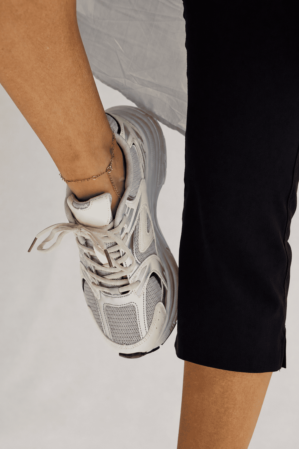 Tênis Victoria Off White no Pé em Vista Superior Tênis Feminino Victoria Off White no pé da modelo, visto de cima, com calça preta, tornozeleira dourada e detalhes em tela e prata.