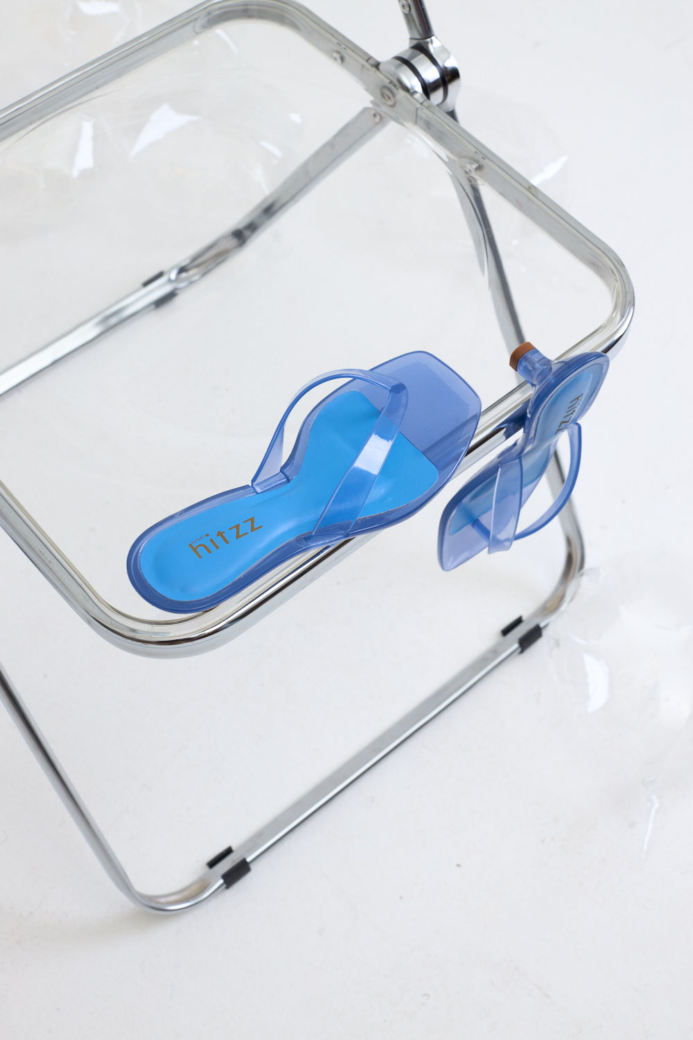 gummy-tamanco-salto-baixo-transparente-azul Par de Tamanco Feminino Flip Flop Gummy azul em PVC translúcido sobre cadeira transparente, vista superior