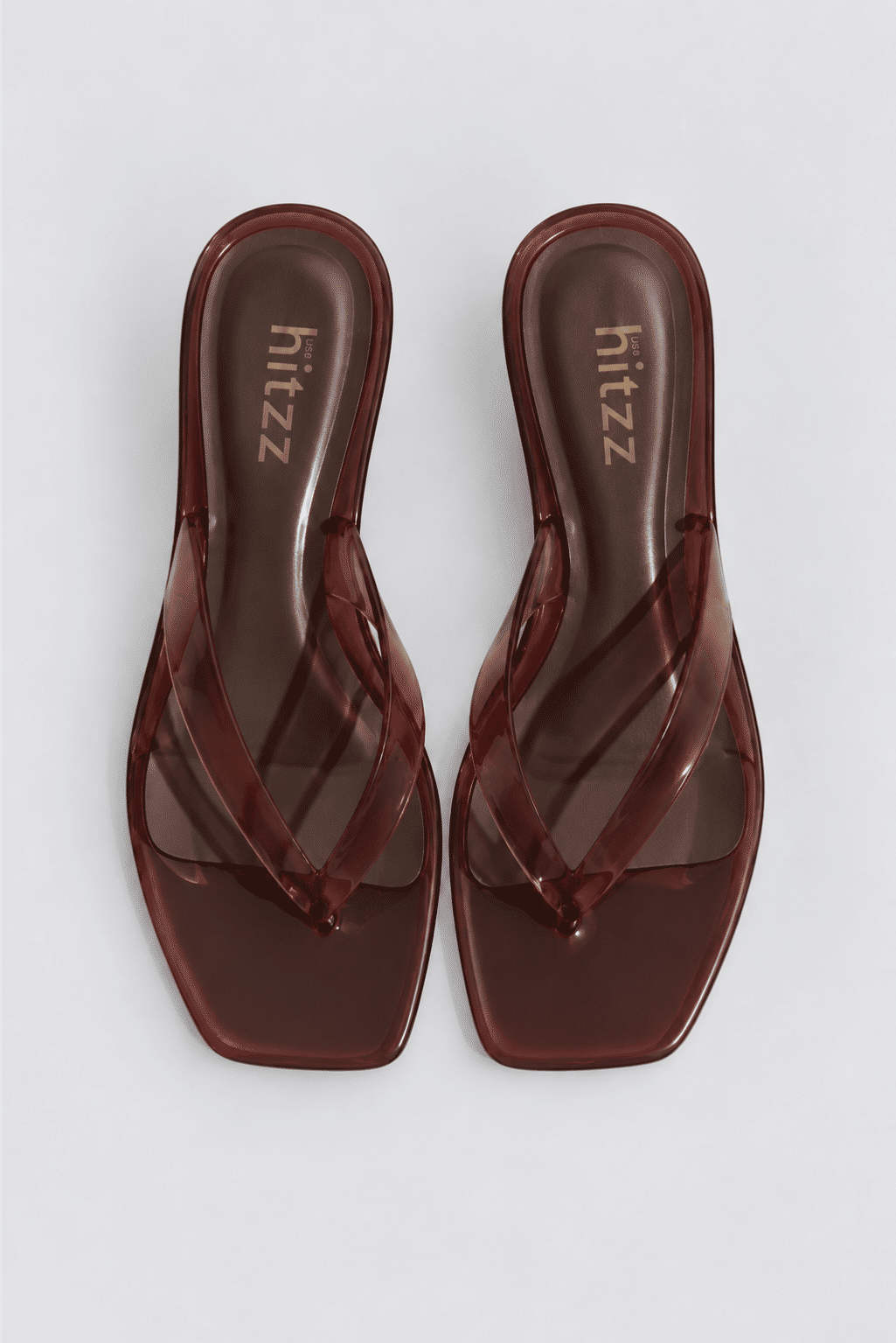 gummy-tamanco-feminino-transparente-salto-baixo-marrom Par do Tamanco Feminino Flip Flop Marrom - Gummy visto de cima, tiras em vinil transparente marrom entrelaçadas e solado quadrado com a marca hitzz na palmilha