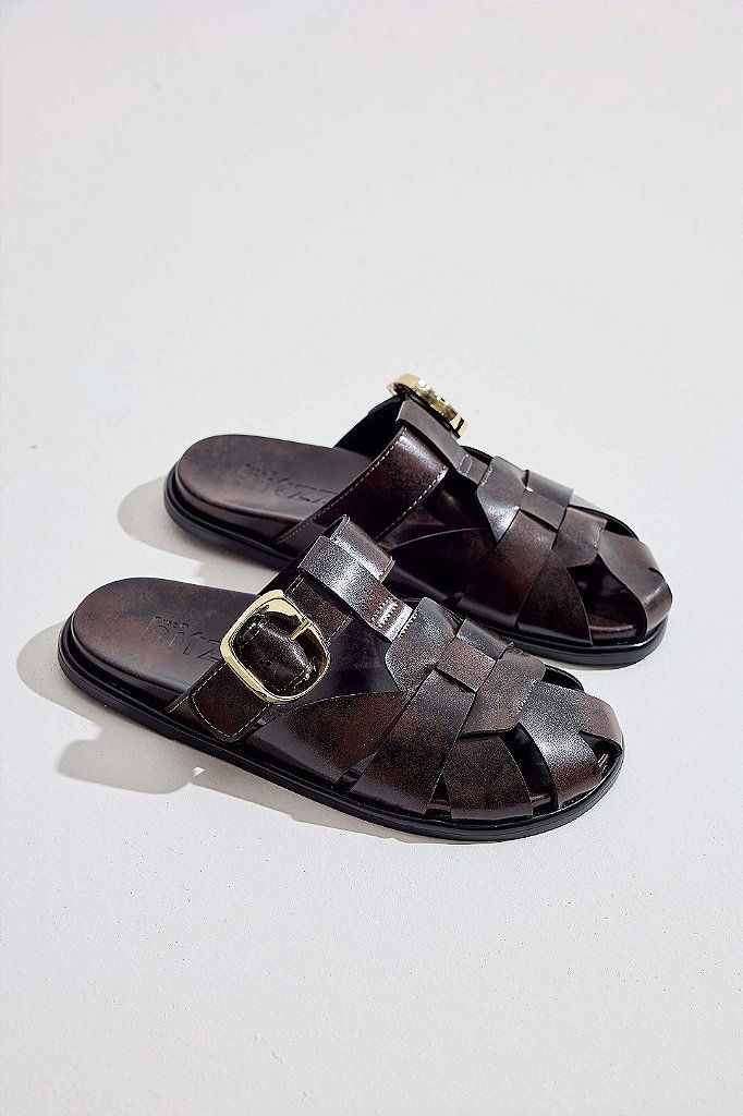 clog-feminino-fivela-marrom-aura Par de clogs marrom com fivela dourada em ângulo, tiras entrelaçadas e sola preta, fundo claro.
