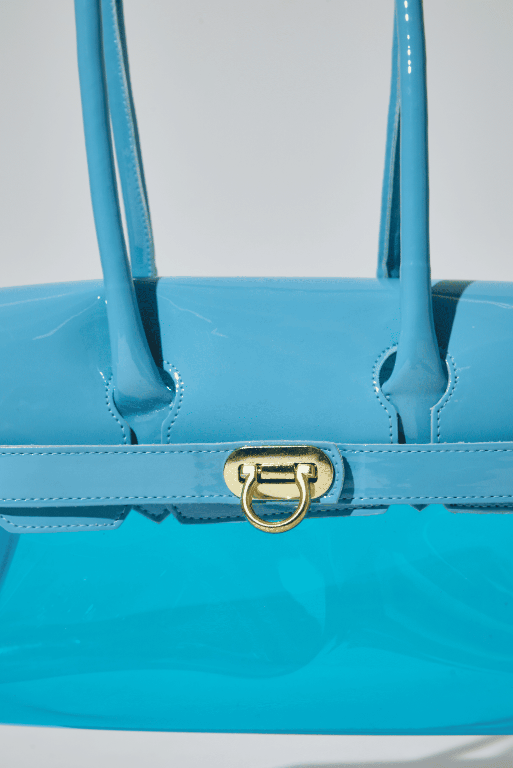 gummy-bolsa-feminina-transparente-verniz-azul-claro Detalhe frontal da Bolsa Feminina Transparente Verniz Gummy azul claro com acabamento em verniz e fecho metálico dourado.