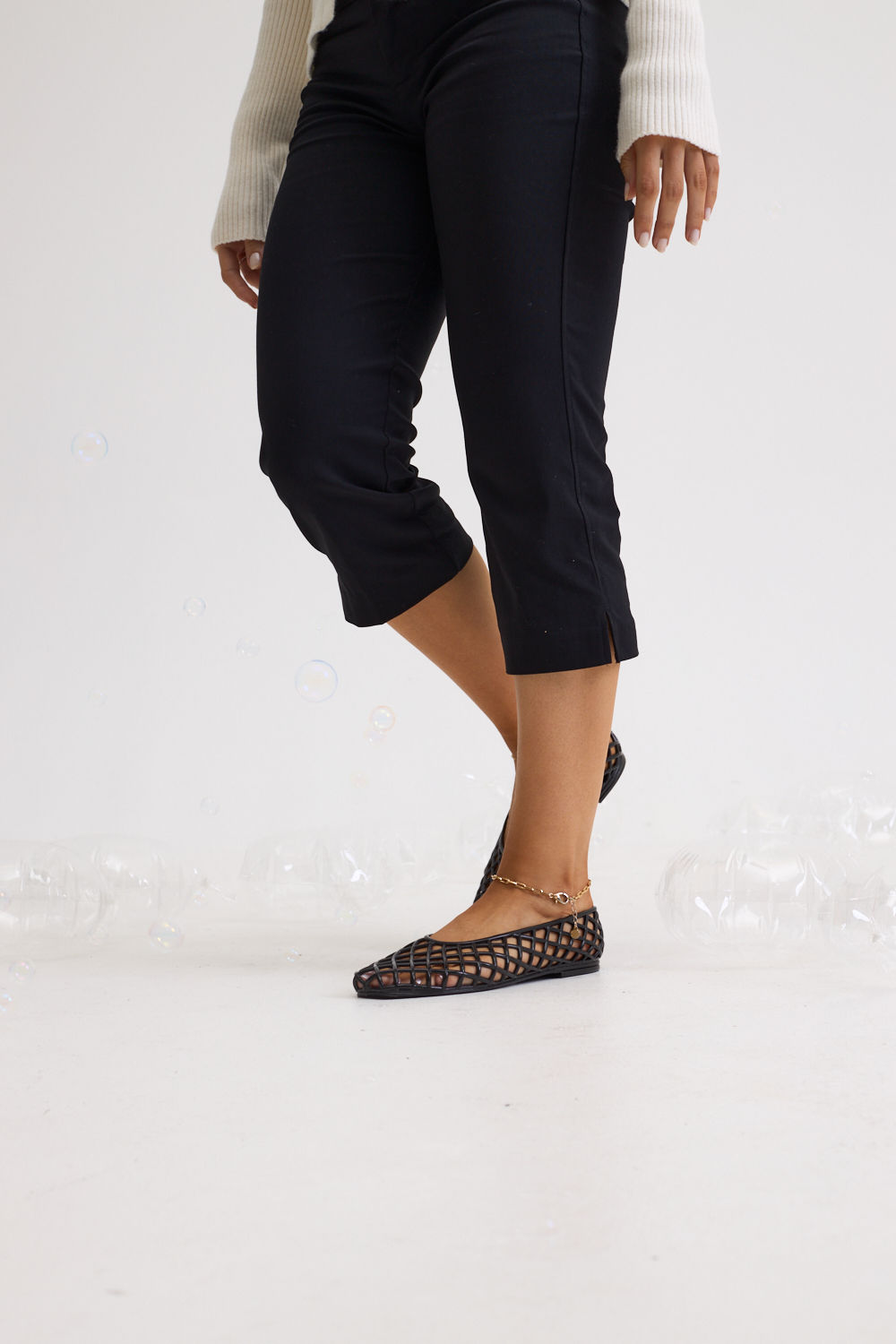 sapatilha-feminina-preto-gummy Closeup dos pés calçados com a Sapatilha Feminina Preto - Gummy em movimento, com calça preta cropped e tricô creme, cenário com bolhas de sabão no chão.