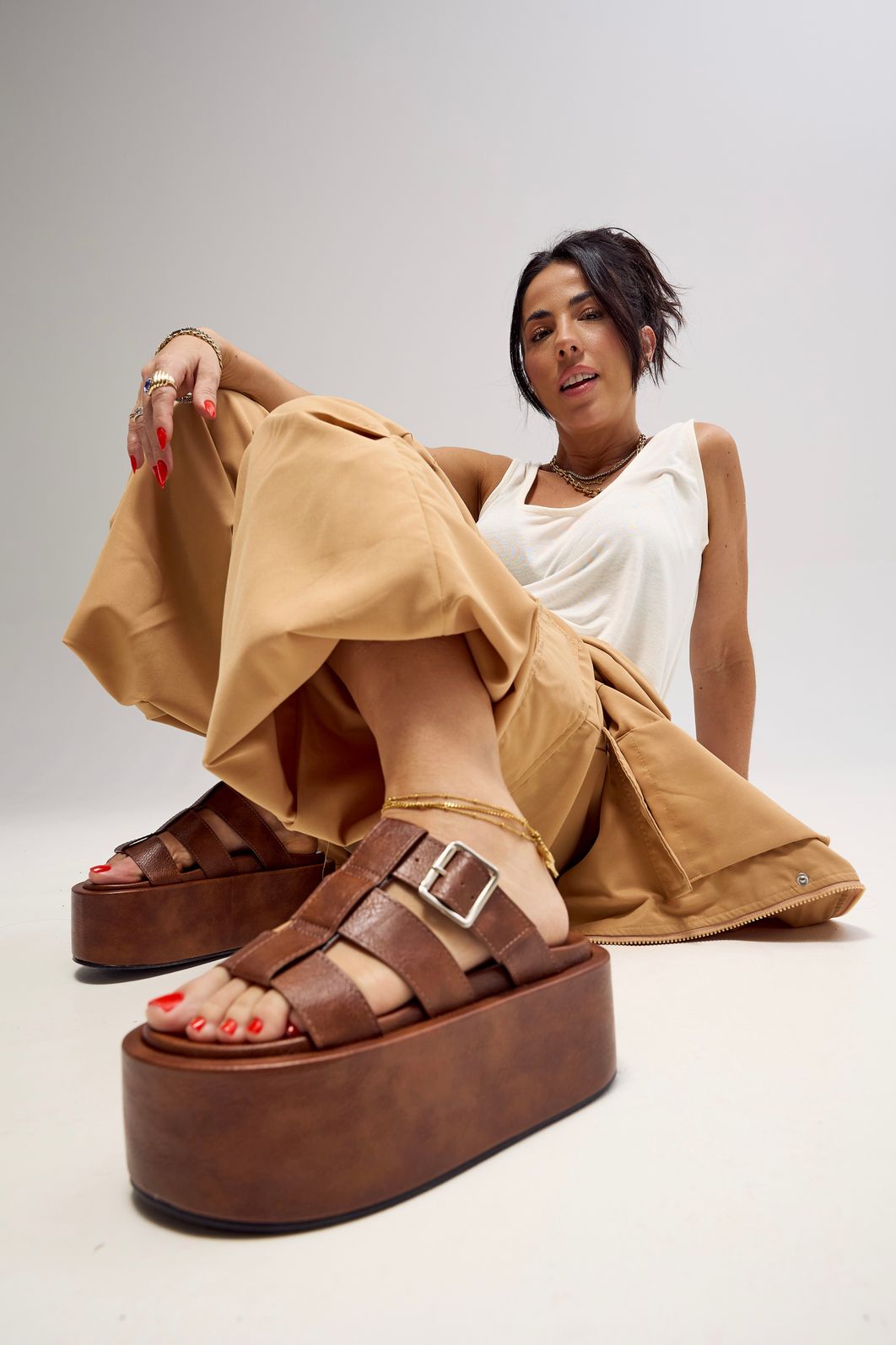 bangkok-tamanco-feminino-camel Modelo sentada no chão, com regata branca e calça bege e tamanco camelfashionista