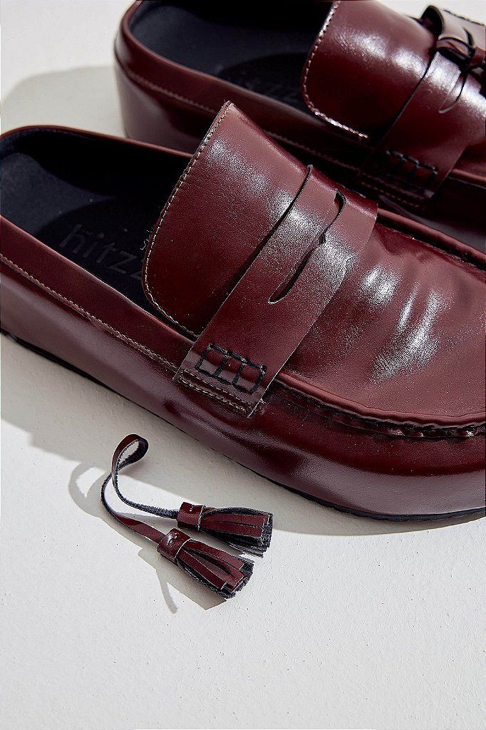 Detalhe aproximado do Clog Mali Bordô com acessório tassel ao lado, fundo preto