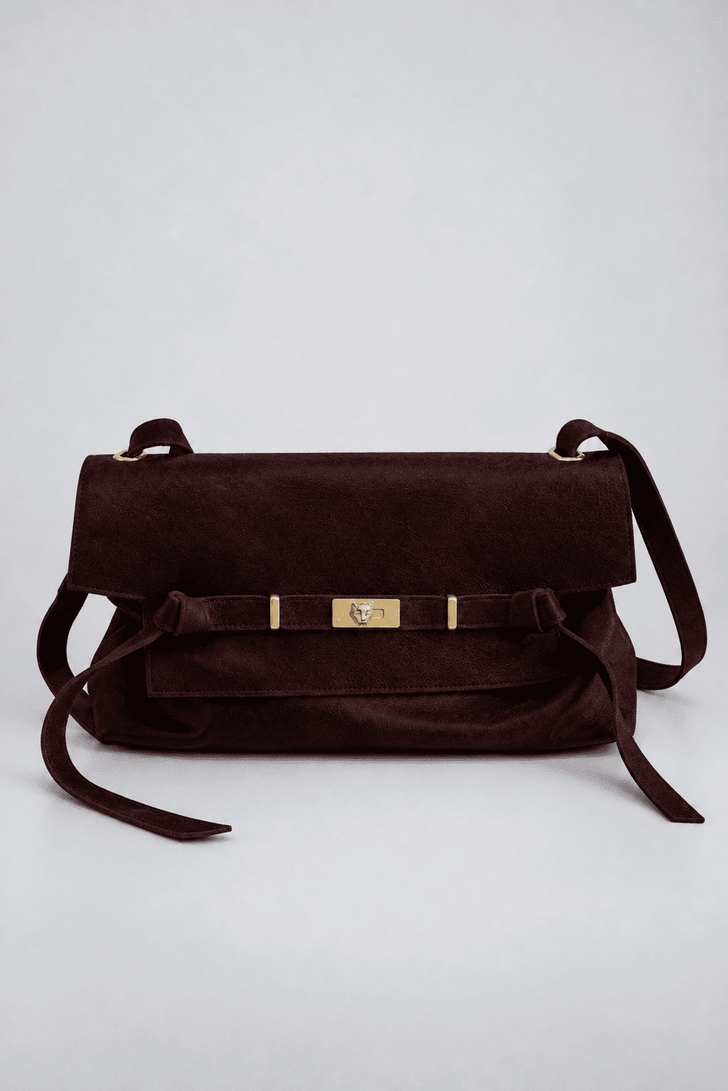 bolsa-feminina-ombro-marrom-vick Bolsa de couro marrom vista de frente, alça ajustável, fecho dourado e tiras laterais soltas, fundo cinza claro.