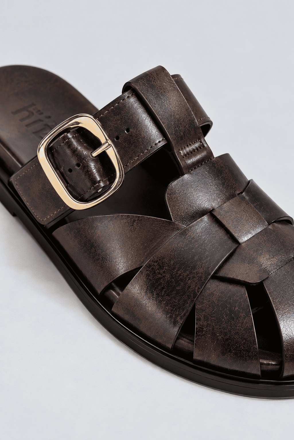 clog-feminino-fivela-marrom-aura Close da fivela dourada e das tiras entrelaçadas do clog marrom, mostrando a palmilha com a marca hitzz.