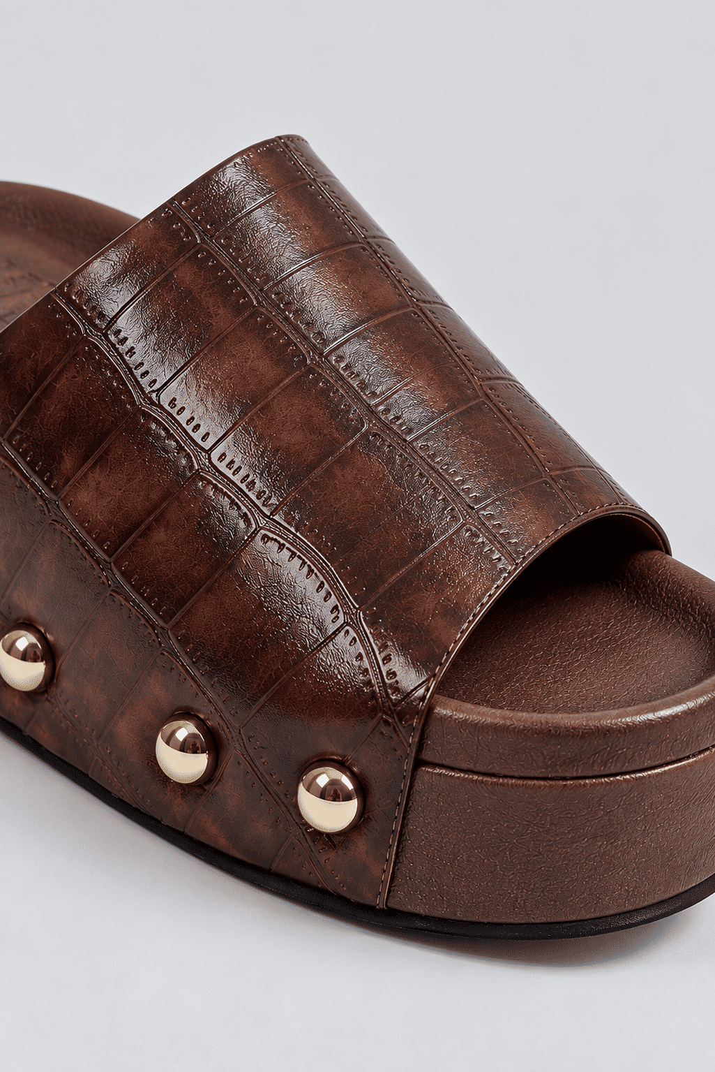 tamanco-feminino-flatform-croco-marrom-lara Close da textura croco marrom e tachas douradas do tamanco flatform Lara