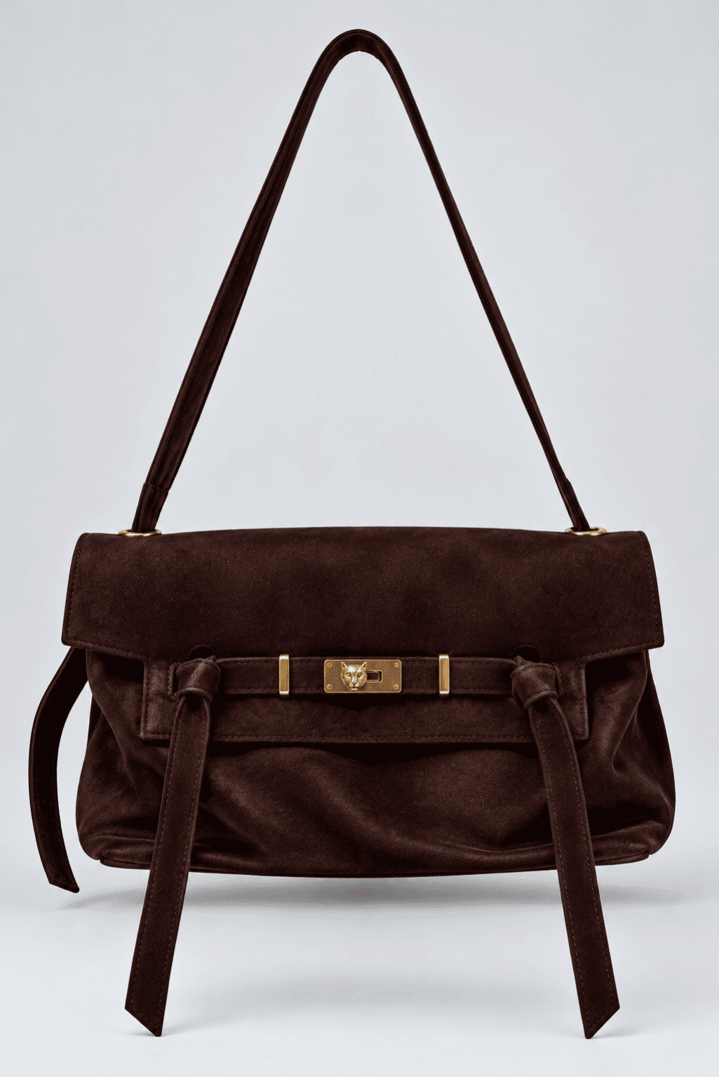 bolsa-feminina-ombro-marrom-vick Bolsa de ombro em couro marrom escuro com fivela dourada e alça longa, isolada em fundo cinza claro.