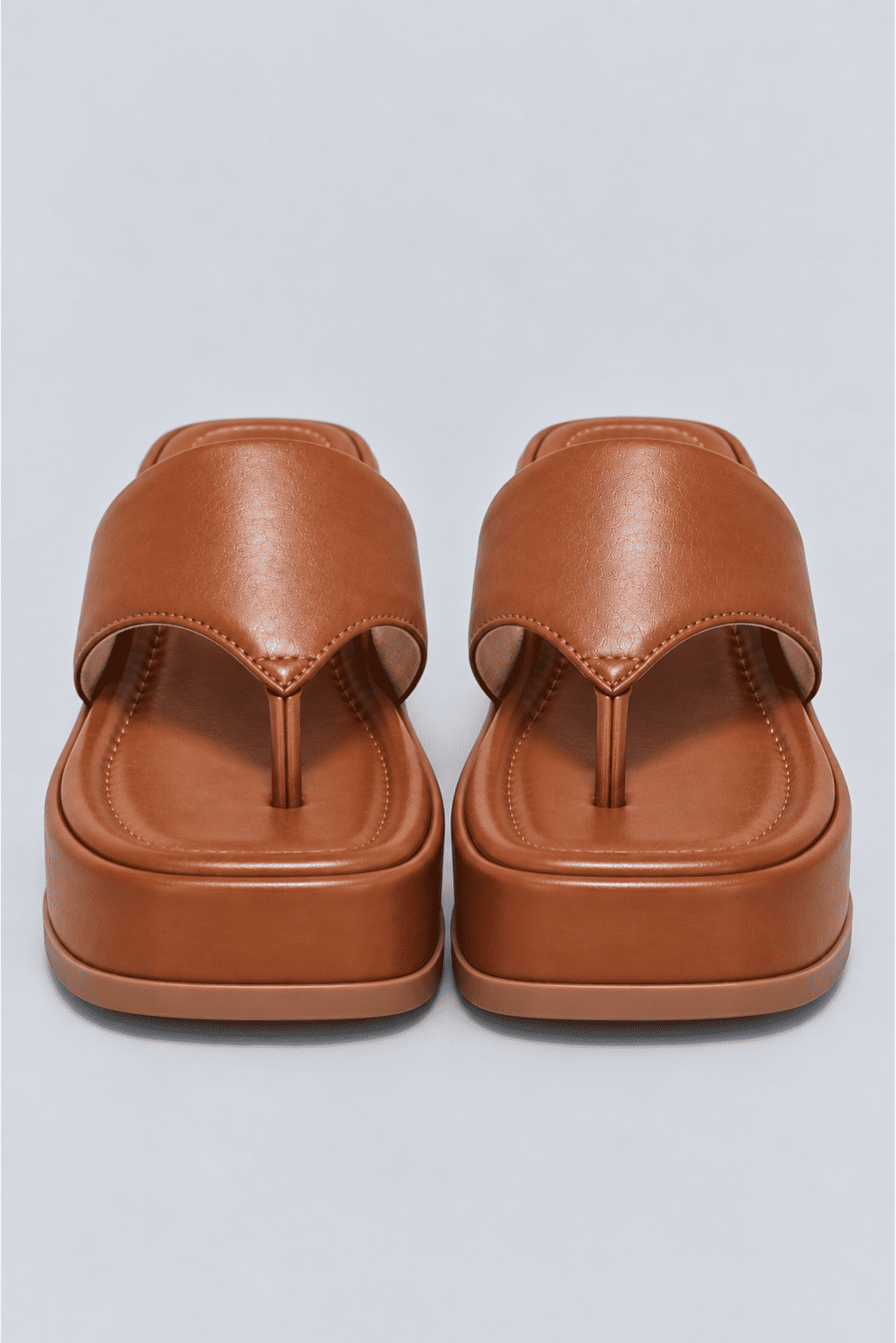 chinelo-flatform-couro-feminino-camel-buzios Par de chinelos flatform camel vistos de frente, mostrando a tira entre os dedos e o solado.