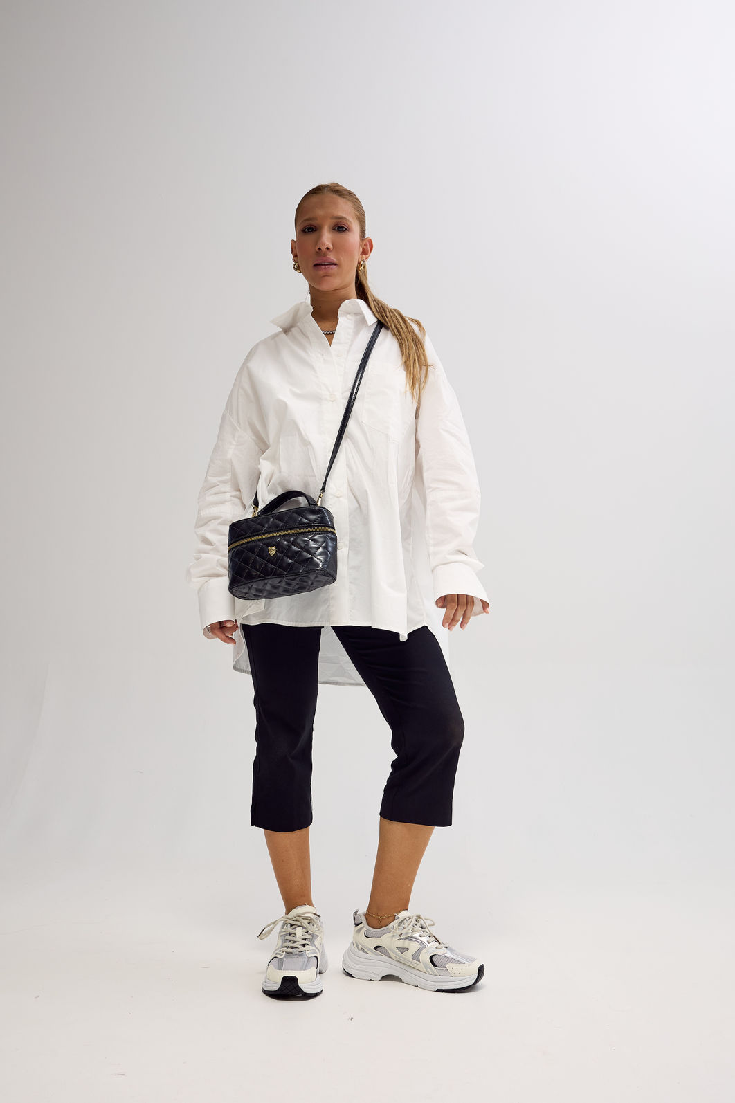 Look completo com Tênis Victoria Off White Modelo de corpo inteiro usando Tênis Feminino Victoria Off White com camisa branca oversized, calça preta cropped e bolsa preta transversal.