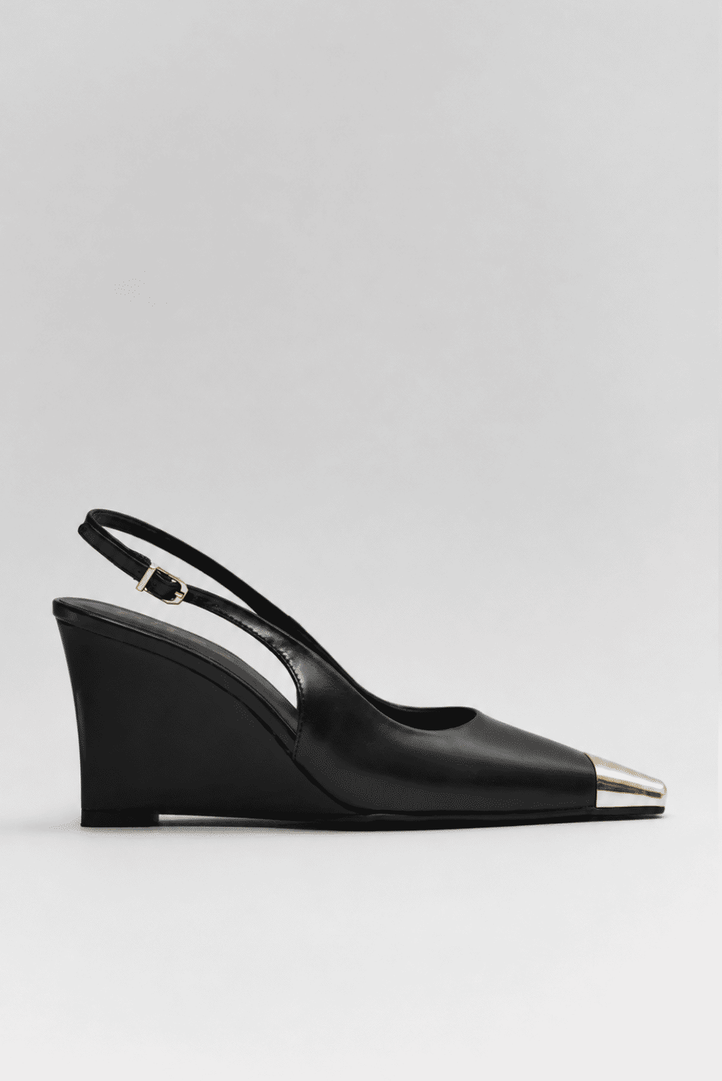 Slingback Feminino Naomi Preto Lateral Slingback feminino Naomi preto em vista lateral, com salto anabela de aproximadamente 9 cm, bico fino com ponteira metálica dourada e tira traseira com fivela ajustável.