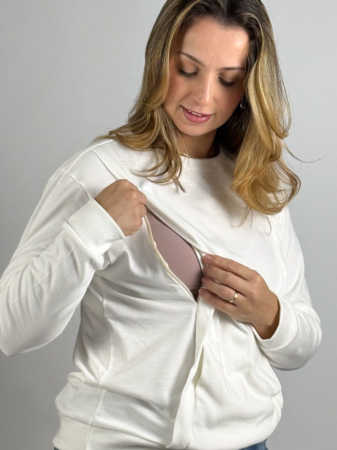 Blusa de amamentação Olívia - Off white Modelo abrindo o zíper de amamentação da blusa Olívia off white, com forro rosado aparente