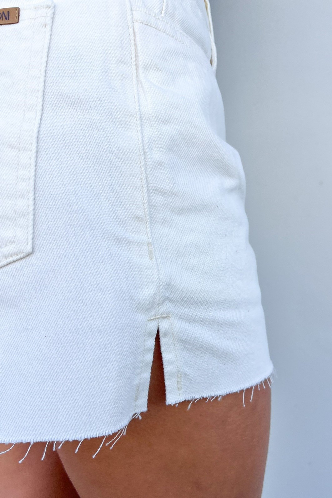 Detalhe da Abertura Lateral em Shorts de Sarja Close-up da lateral do Shorts Bling, destacando a pequena abertura na perna e a textura da sarja 100% algodão.