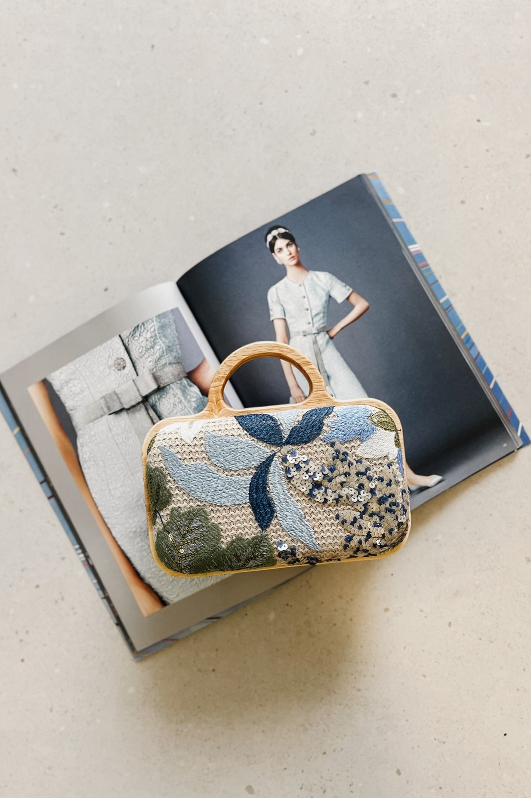 Clutch Flora Azul com as duas opções de alça: a de mão em madeira e a alça longa de corrente dourada ao lado, mostrando sua versatilidade.