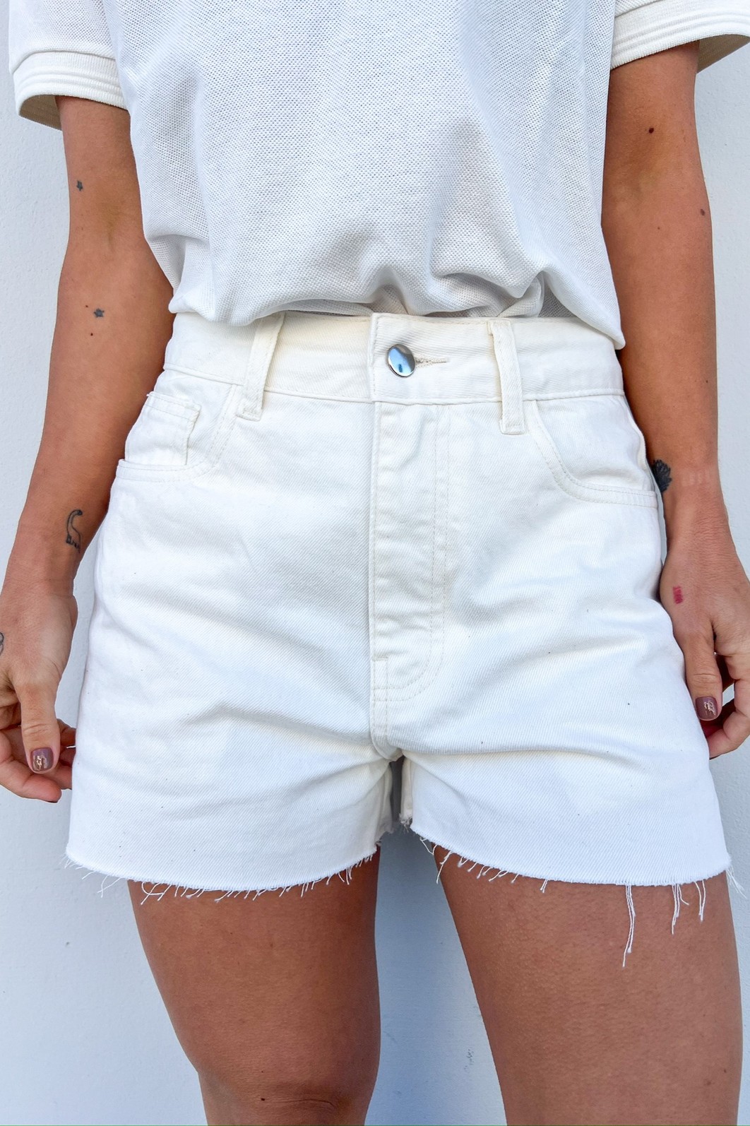 Look de Verão com Shorts Branco 100% Algodão Modelo vestindo o Shorts de Sarja Bling na cor Branco Off, mostrando a modelagem reta e o detalhe da bainha desfiada.