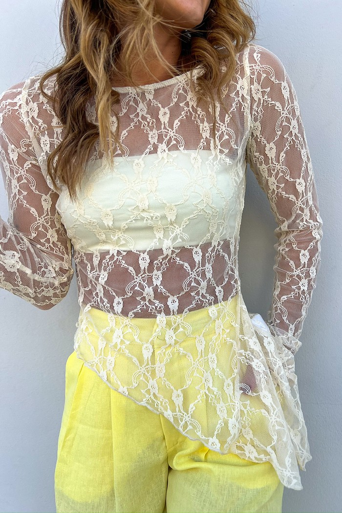 Blusa de Renda Manga Longa Assimétrica em Tom Areia Modelo vestindo a Blusa de Renda Assimétrica Sofia Areia, destacando a transparência elegante da renda.