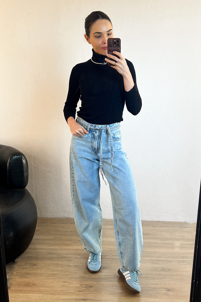 modelo em frente ao espelho usando calça jeans estilo ballon com blusa de gola alta preta 