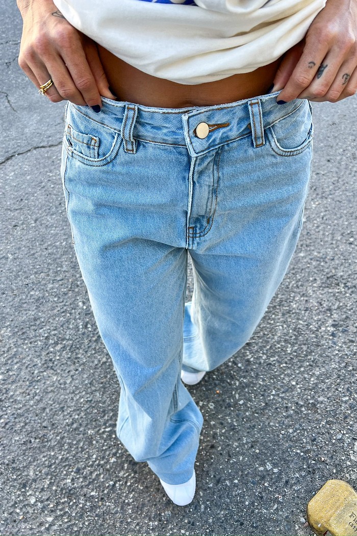Calça Jeans Feminina Wide Leg com Lavagem Clara Detalhe da Calça Jeans Wide Leg Vicky, focando na textura do jeans 100% algodão, na cor clara e no fechamento com botão e zíper na cintura.