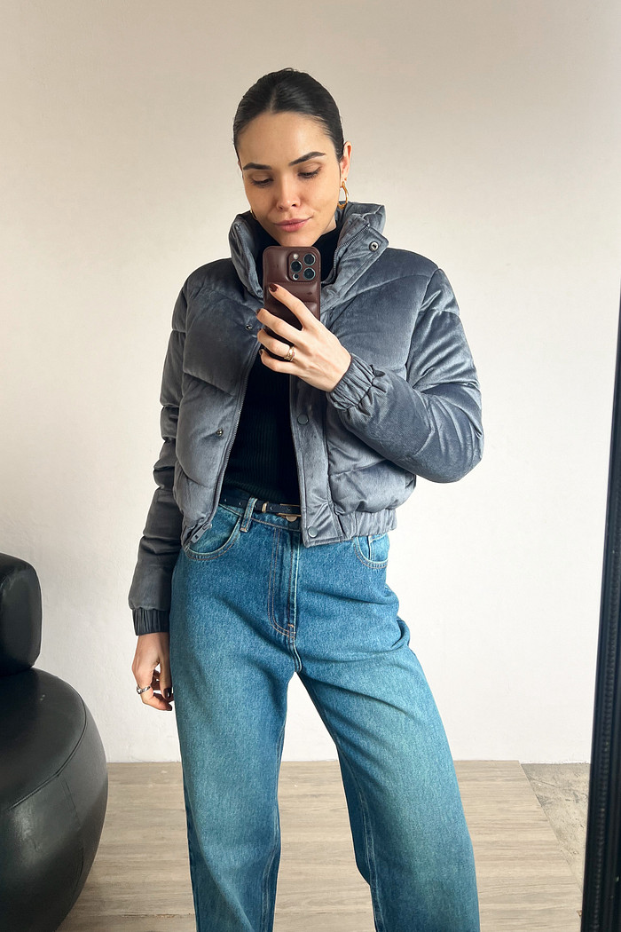 modelo usando jaqueta puffer cinza azulado com calça jeans e blusa preta em frente ao espelho