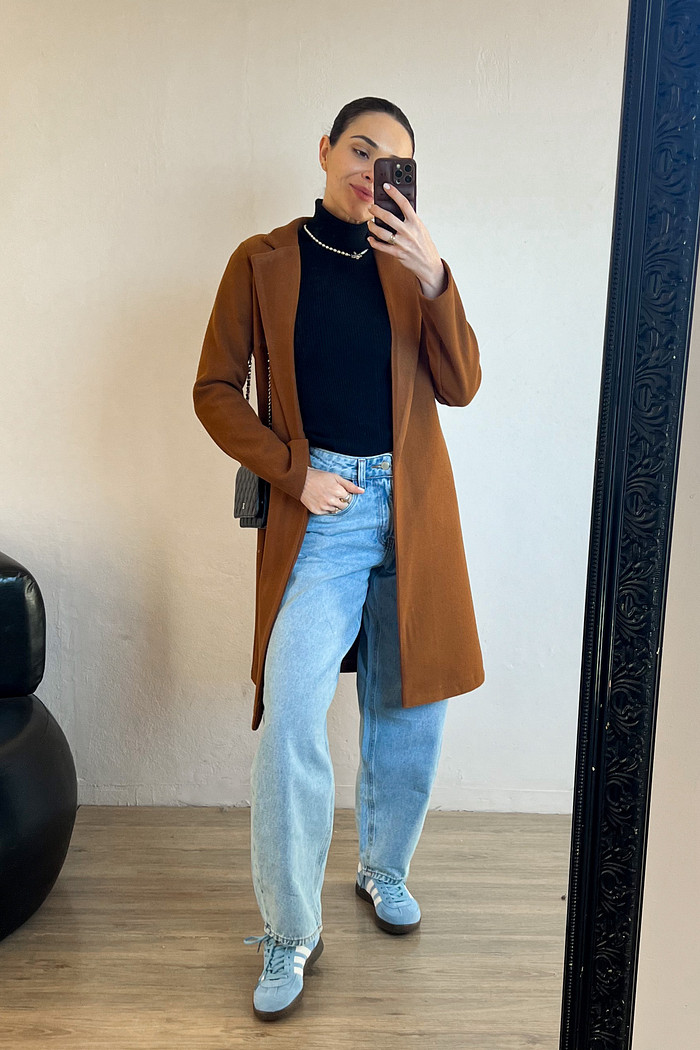 modelo em frente ao espelho usando calça jeans claro com blusa suiça preta de manga longa e gola alta com sobretudo caramelo de lã batida por cima