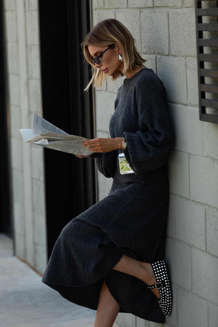 modelo encostada na parete usando conjunto cinza escuro de blusa de manga balão e saia midi