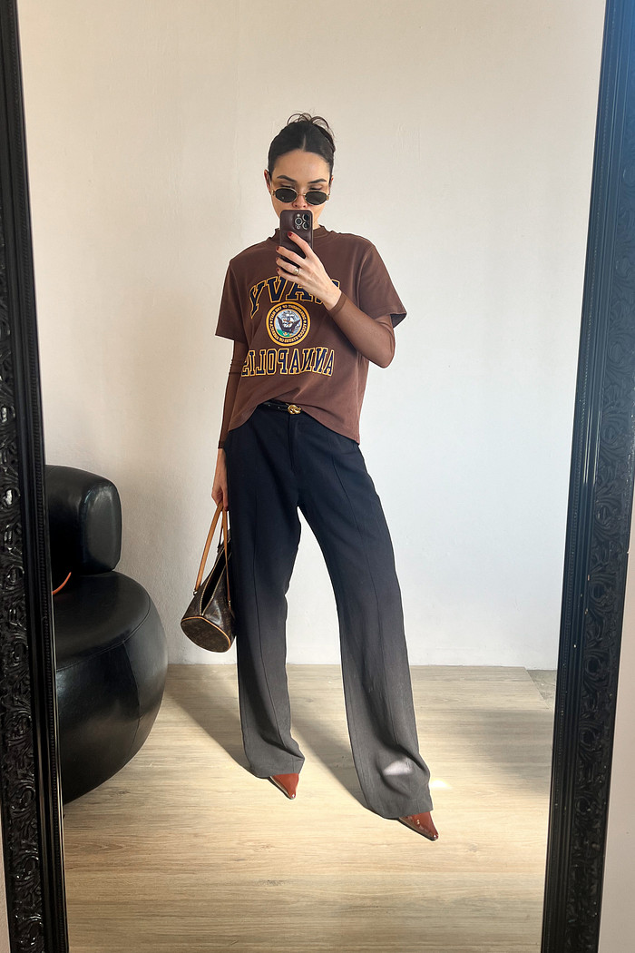 Modelo em frente ao espelho usando blusa de manga curta marrom e calça preta de alfaiataria