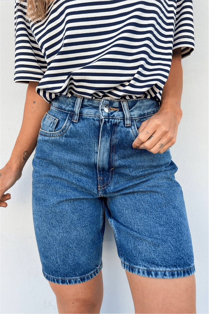 Bermuda Jeans de Cintura Alta e Corte Reto Dark Blue Modelo vestindo a Bermuda Jeans Mom Lia na cor dark blue, mostrando a cintura alta e o comprimento mais alongado da peça.