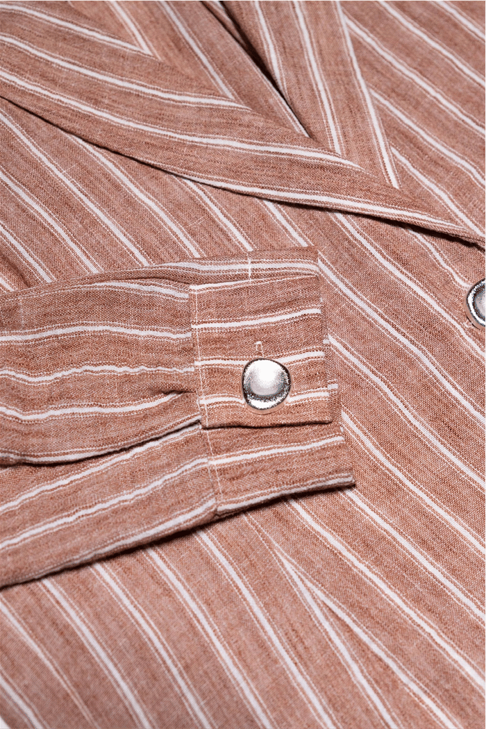 Detalhe do Botão Prateado no Blazer de Listras Abby Close-up do punho do Blazer Camisa de Listras Abby, destacando o design único e o brilho do botão prateado sobre o tecido listrado.