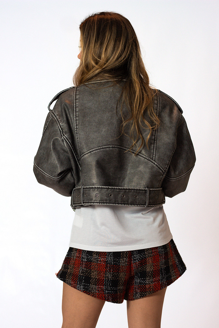 Foto de costas da modelo vestindo jaqueta de couro estonada cinza, mostrando os detalhes da jaqueta