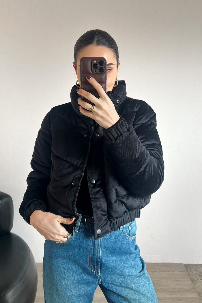 Modelo vestindo jaqueta puffer preta de tecido cotele em frente ao espelho 