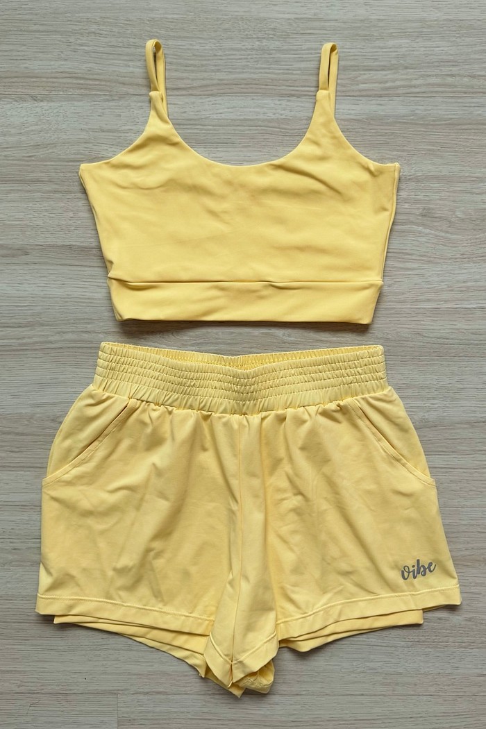 Modelo vestindo o Conjunto Top e Shorts Mel na cor amarelo suave, com top cropped de alças finas e shorts de cós alto confortável.