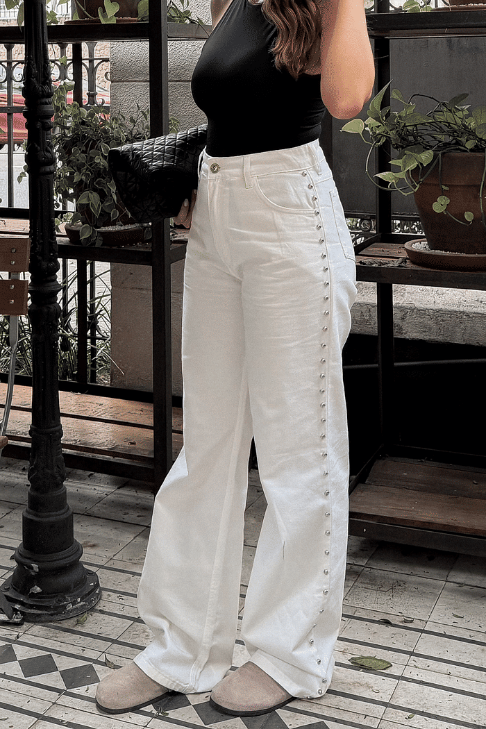Calça wide leg off white em sarja com taxas prateadas aplicadas na lateral e cintura alta.