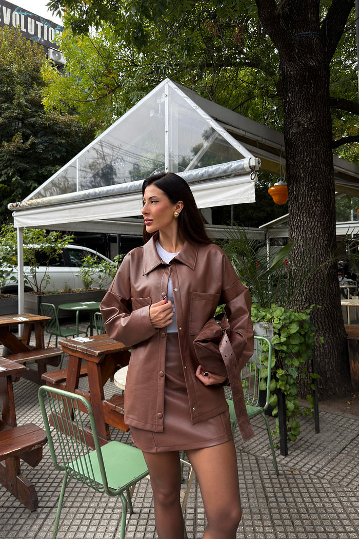Camisa feminina marrom em poliuretano com bolsos frontais e modelagem ampla, visual sofisticado tipo couro, usada em look urbano moderno com saia coordenada