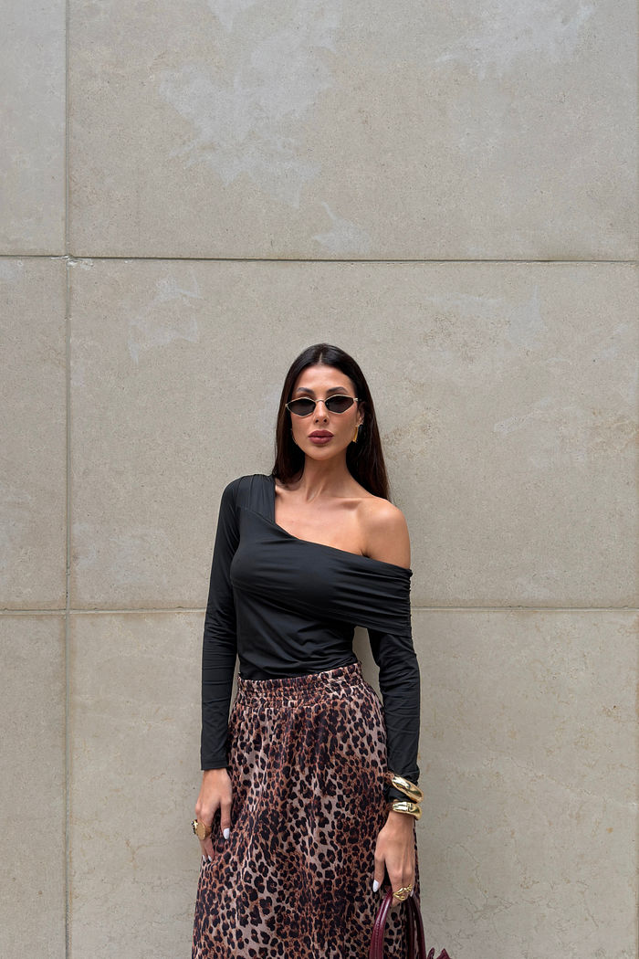 Blusa preta com decote assimétrico, drapeado caindo no ombro e mangas longas franzidas.