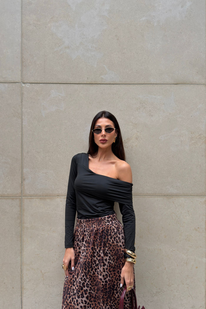 Blusa preta com decote assimétrico, drapeado caindo no ombro e mangas longas franzidas.