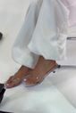 gummy-tamanco-feminino-transparente-salto-baixo Tamanco Feminino Flip Flop Gummy transparente nos pés da modelo com calça branca em look casual