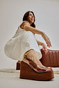 kourtney-sandália-feminina-plataforma-vinil-camel Modelo usando Sandália Kourtney camel com plataforma alta, vinil transparente e solado amadeirado