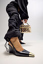 Close Slingback Naomi Preto Close da modelo usando slingback feminino Naomi preto com salto anabela de 9 cm e bico metálico dourado, acompanhado de bolsa metalizada dourada.