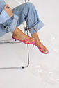 gummy-tamanco-feminino-translucido-rosa Tamanco Feminino Flip Flop Gummy rosa em PVC translúcido, modelo sentada em cadeira transparente com as pernas cruzadas