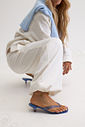 gummy-tamanco-salto-baixo-transparente-azul Tamanco Feminino Flip Flop Gummy azul em PVC translúcido, modelo agachada ajustando a tira do calçado