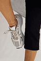 Tênis Victoria Off White no Pé em Vista Superior Tênis Feminino Victoria Off White no pé da modelo, visto de cima, com calça preta, tornozeleira dourada e detalhes em tela e prata.