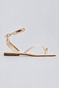 sandalia-rasteira-feminina-de-dedo-off-white-nati Sandália rasteira feminina de dedo off white com tira no tornozelo e detalhes dourados, vista lateral em fundo cinza claro.