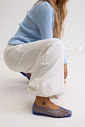 sapatilha-feminina-azul-gummy Modelo agachada usando a Sapatilha Feminina Azul - Gummy com tricô canelado azul claro e calça wide leg em tom creme, tornozeleira dourada com pingente.