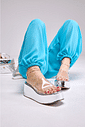tamanco-flatform-feminino-tira-vinil-prata Adele - Tamanco Flatform Feminina Tira Vinil Prata nos pés da modelo sentada no chão, pernas esticadas com calça azul